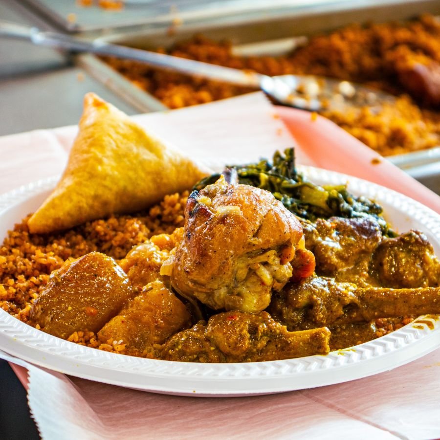 Chicken and jollof rice platter with samosa and greens, served family-style