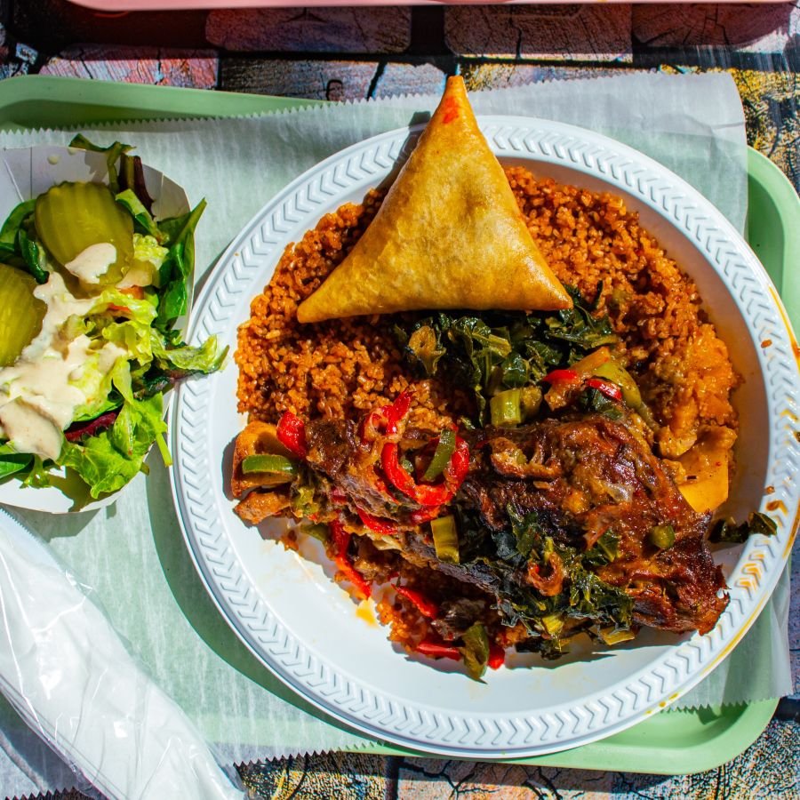 Plate of jollof rice with braised greens, a samosa and a side salad